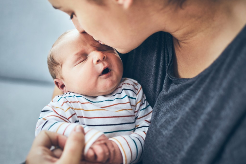 Eine Mutter küsst ihr neugeborenes Baby auf die Stirn.