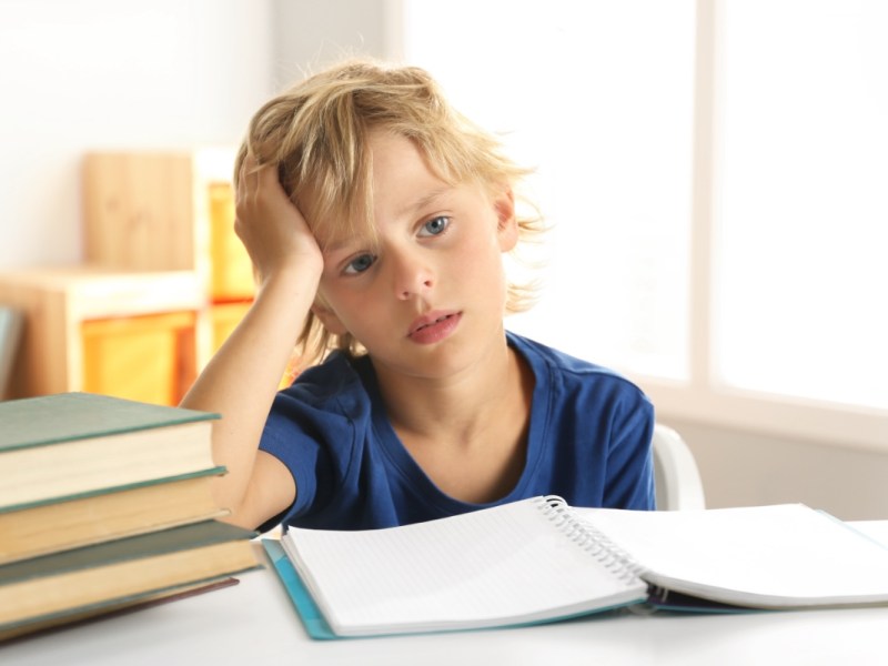 Ein nachdenklicher kleiner, blonder Junge sitzt an seinen Hausaufgaben für die Schule.