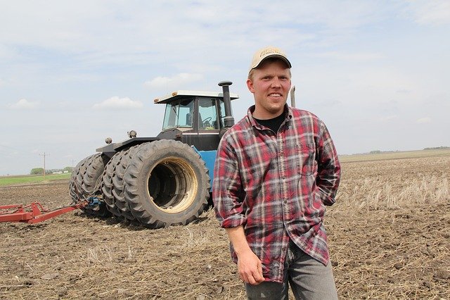 Ein Bauer steht auf einem Feld vor seinem Traktor.