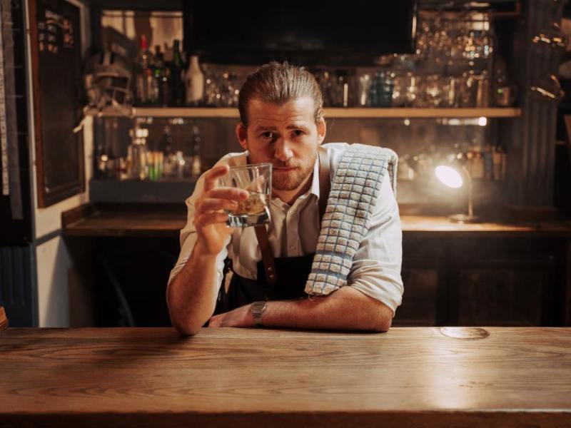 Ein junger Wirt trinkt hinter seinem Tresen einen Whiskey nach Feierabend.