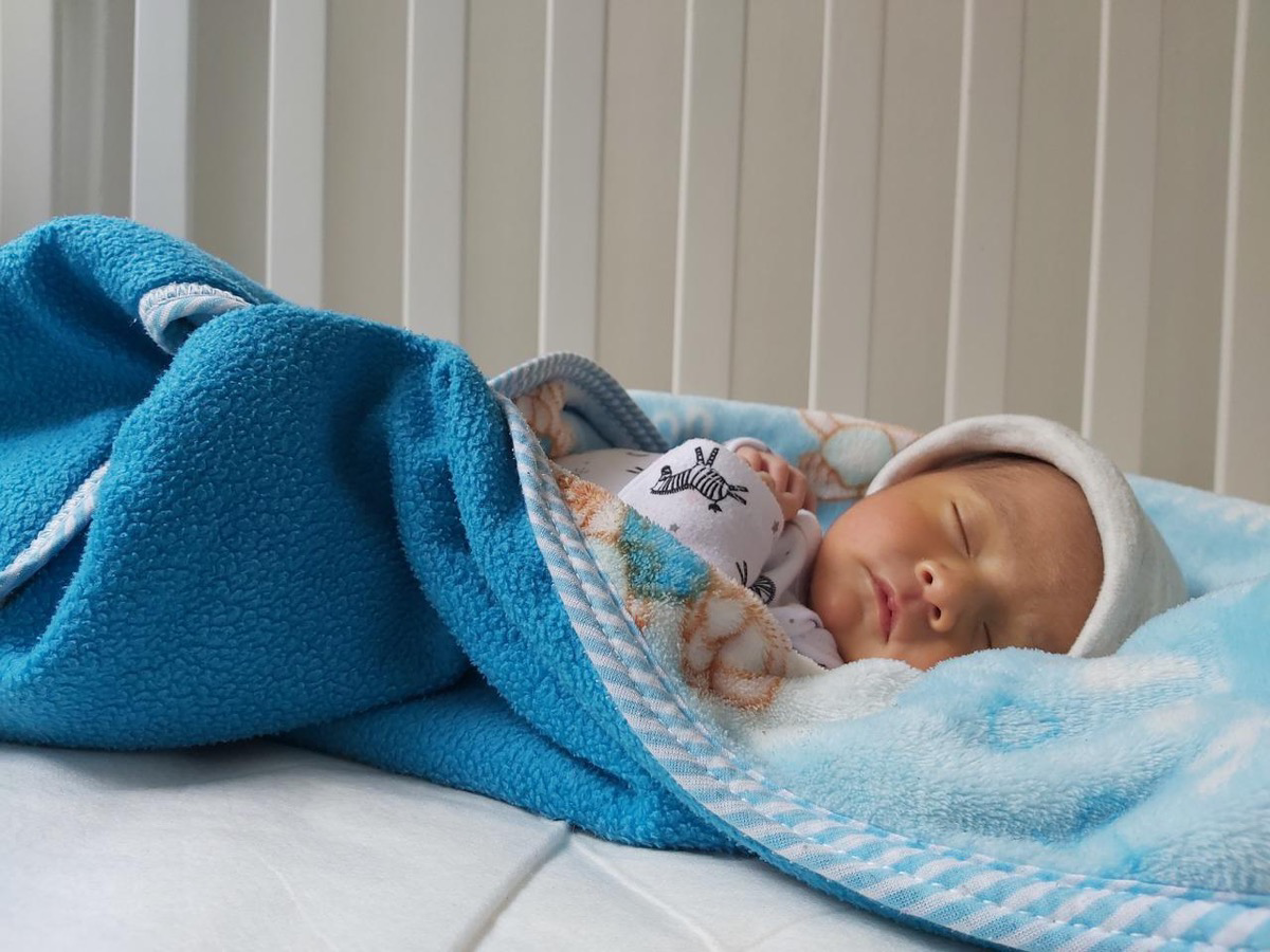 Ein schlafendes Baby liegt zugedeckt im Bett