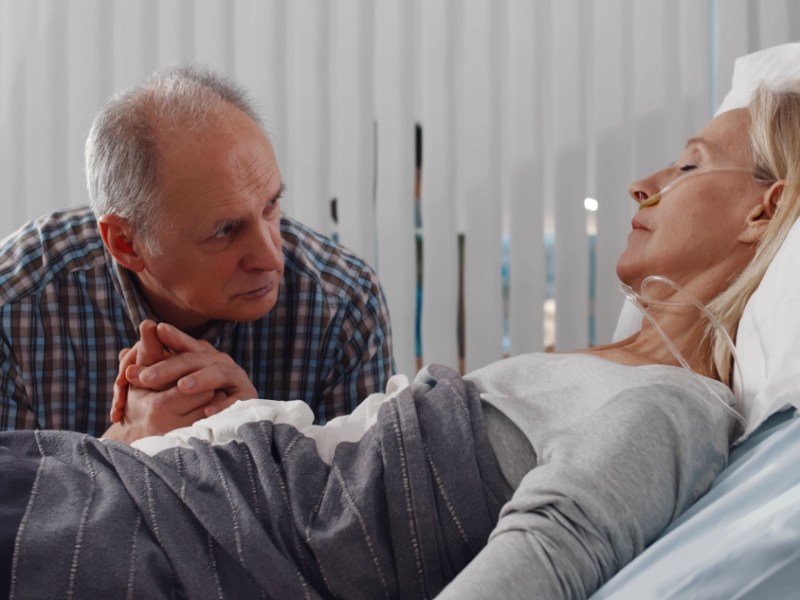 Ein älterer Mann besucht seine Frau im Krankenhaus und hält ihre Hand.