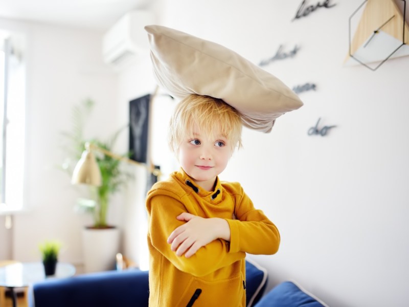 Ein kleiner Junge hat ein Kissen auf dem Kopf und lächelt.