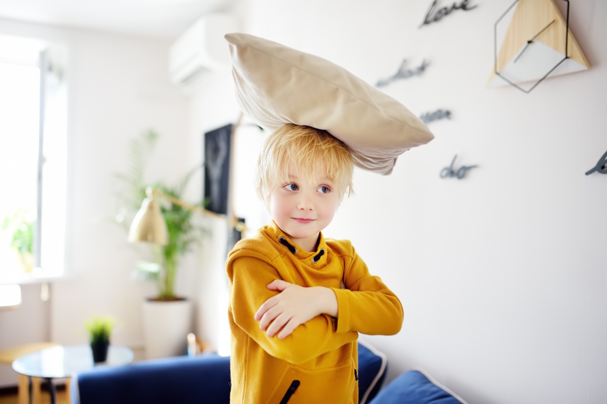 Ein kleiner Junge hat ein Kissen auf dem Kopf und lächelt.